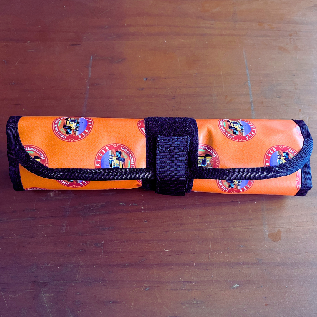 A Desert Dog tool or cutlery roll, rolled up and closed with a velcro tabl. The roll is made with heavy strong vinyl and features the Desert Dog signature branding.