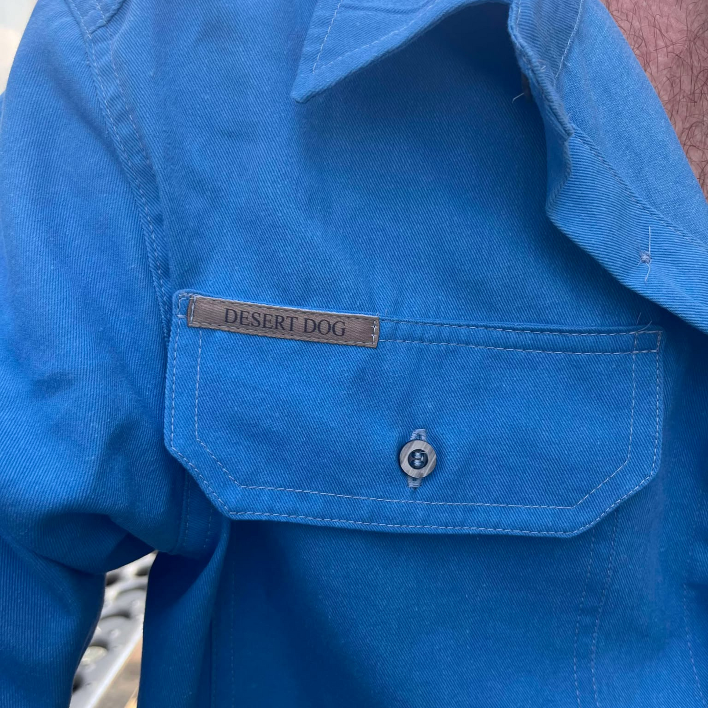 Front pocket detail of a blue Desert Dog WorkTough shirt showing the pocket with buttoned flap and label