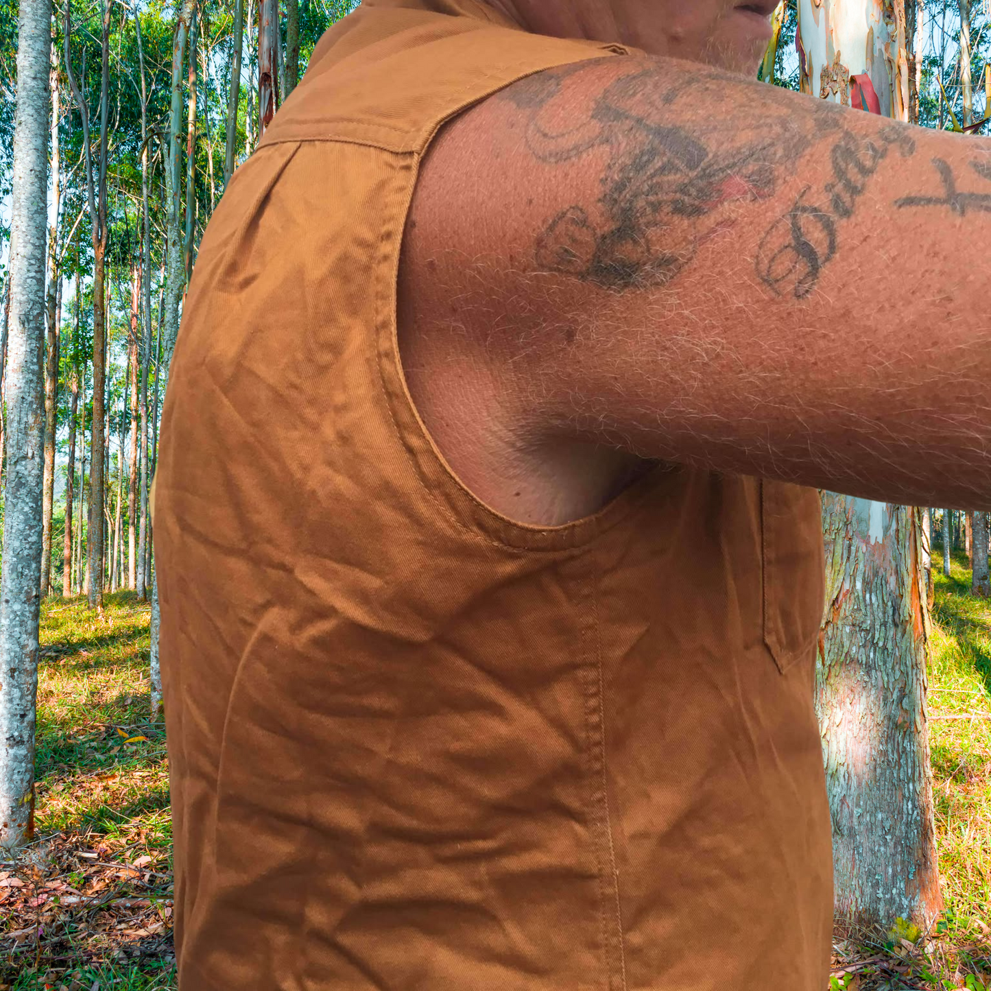 A male wearing a rust coloured DesertDog WorkTough shirt showing the armhole and side detaill. He is standing in a eucalypt bush area.