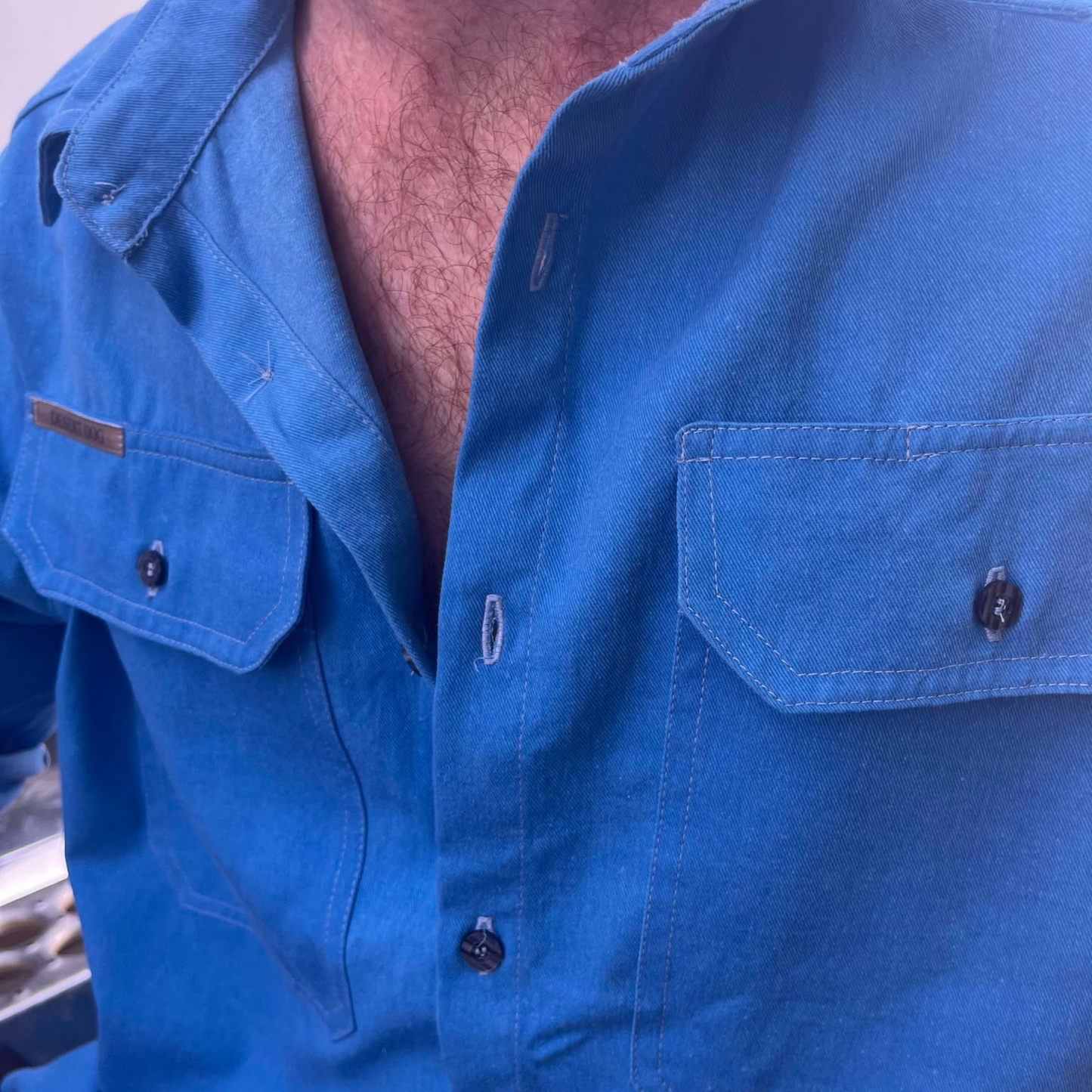 A closeup detailed photo of the chest area of a blue Desert Dog WorkTough shirt featuring pocket and button detail.