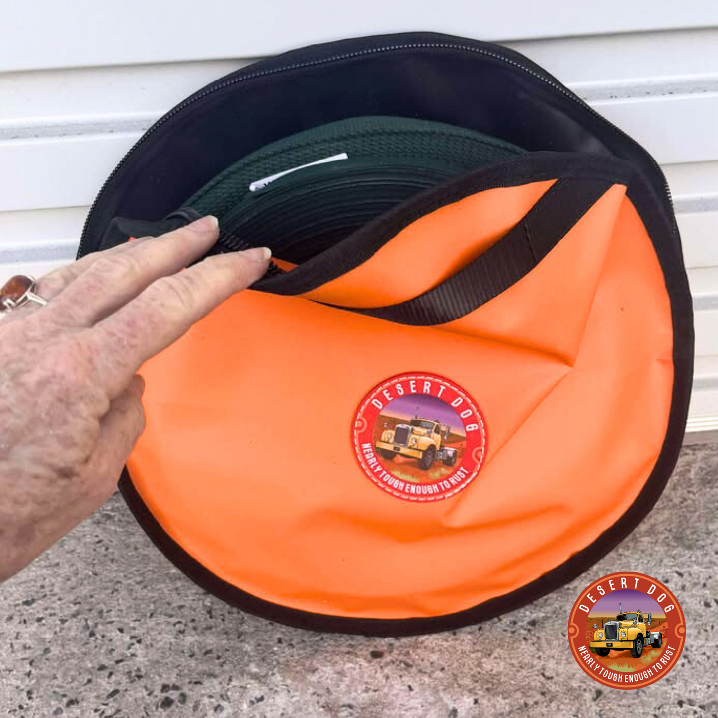 Orange desert dog rope bag with a desert dog logo leaning against a shed rolladoor. A person is holding the bag open to reveal a roll of something coiled inside.