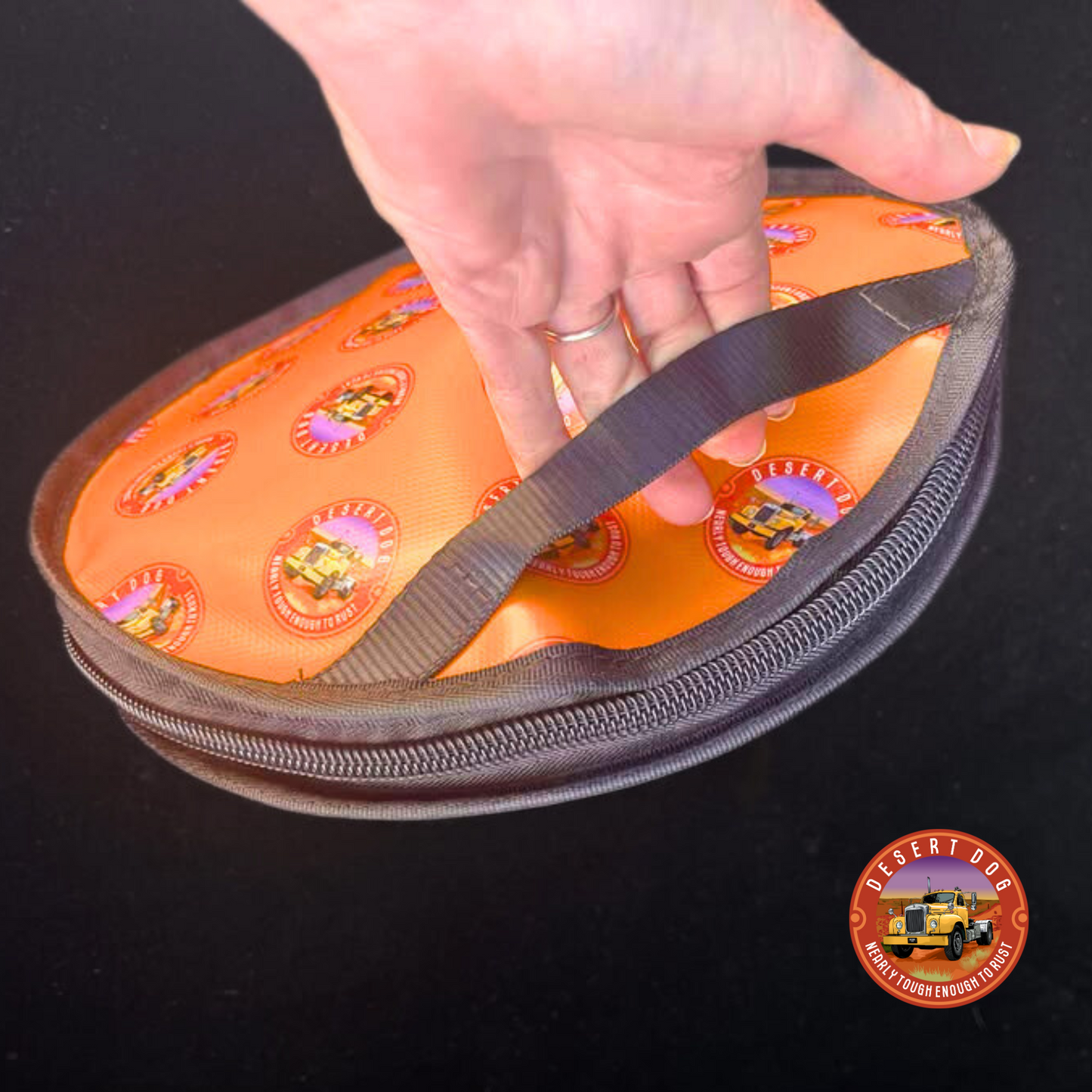 Hand holding an orange Desert Dog logo rope bag with an easy-grab carry strap.