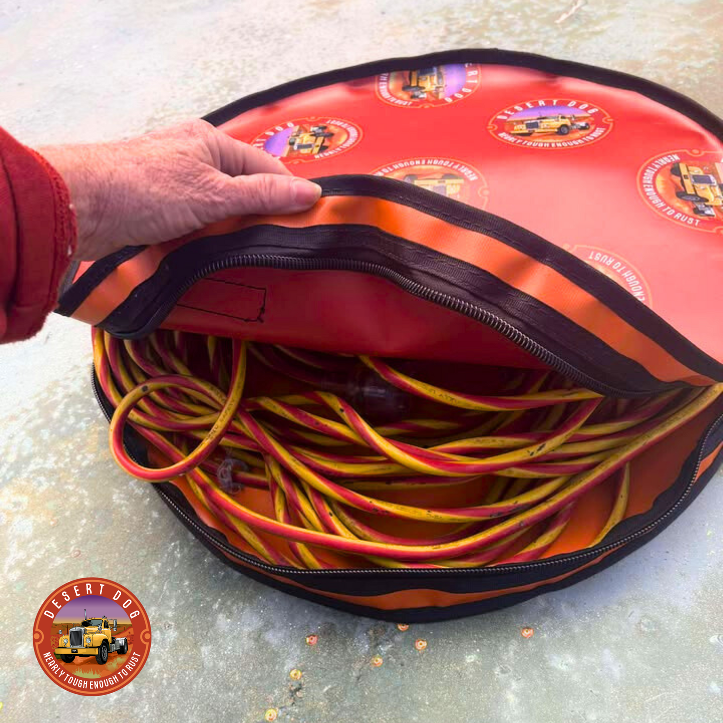 Rust coloured rope bag with Desert Dog logo allover, containing a coiled yellow and red cable, held open by a person.