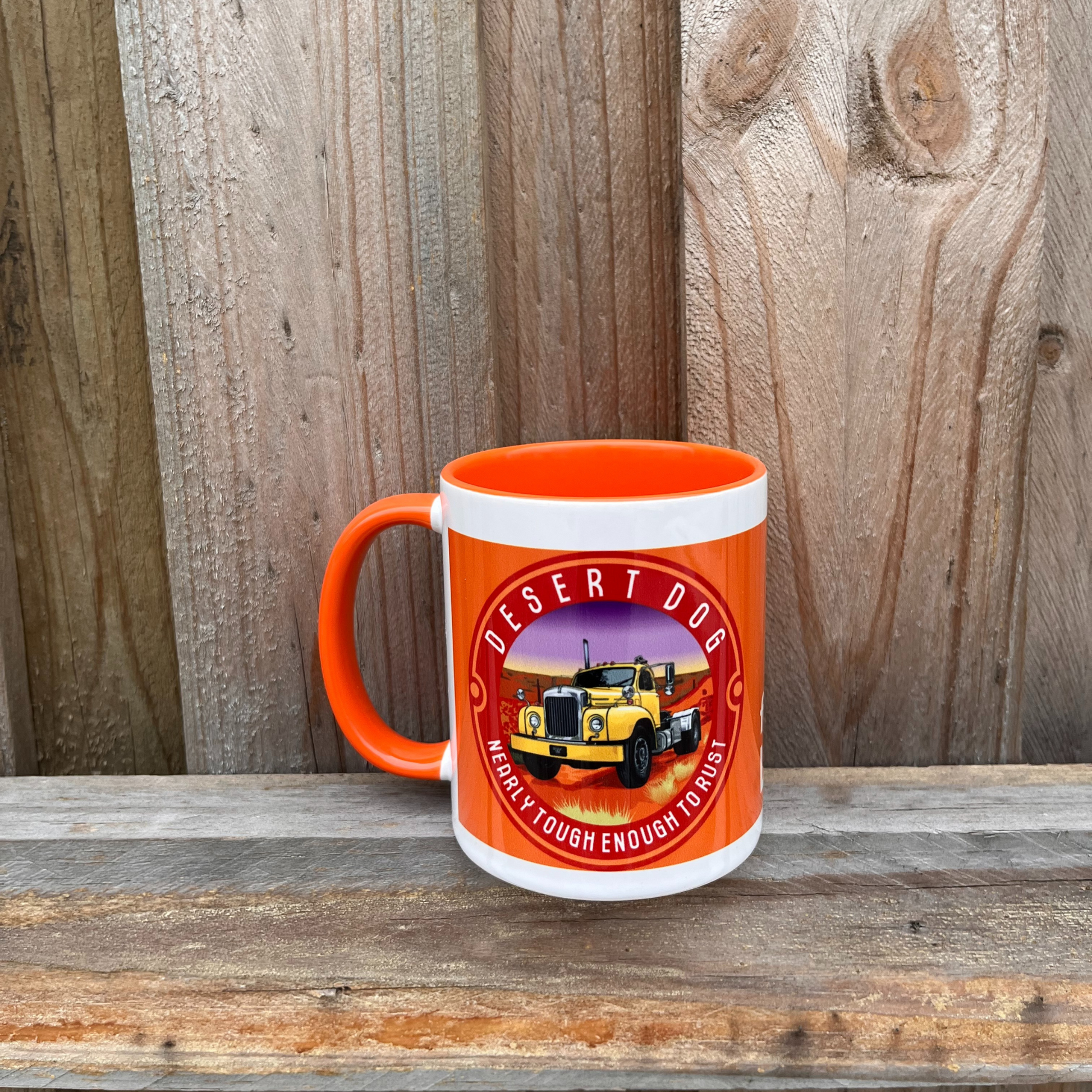 An orange and white coffee mug on a wooden fence featuring the Desert Dog B model Mack truck logo