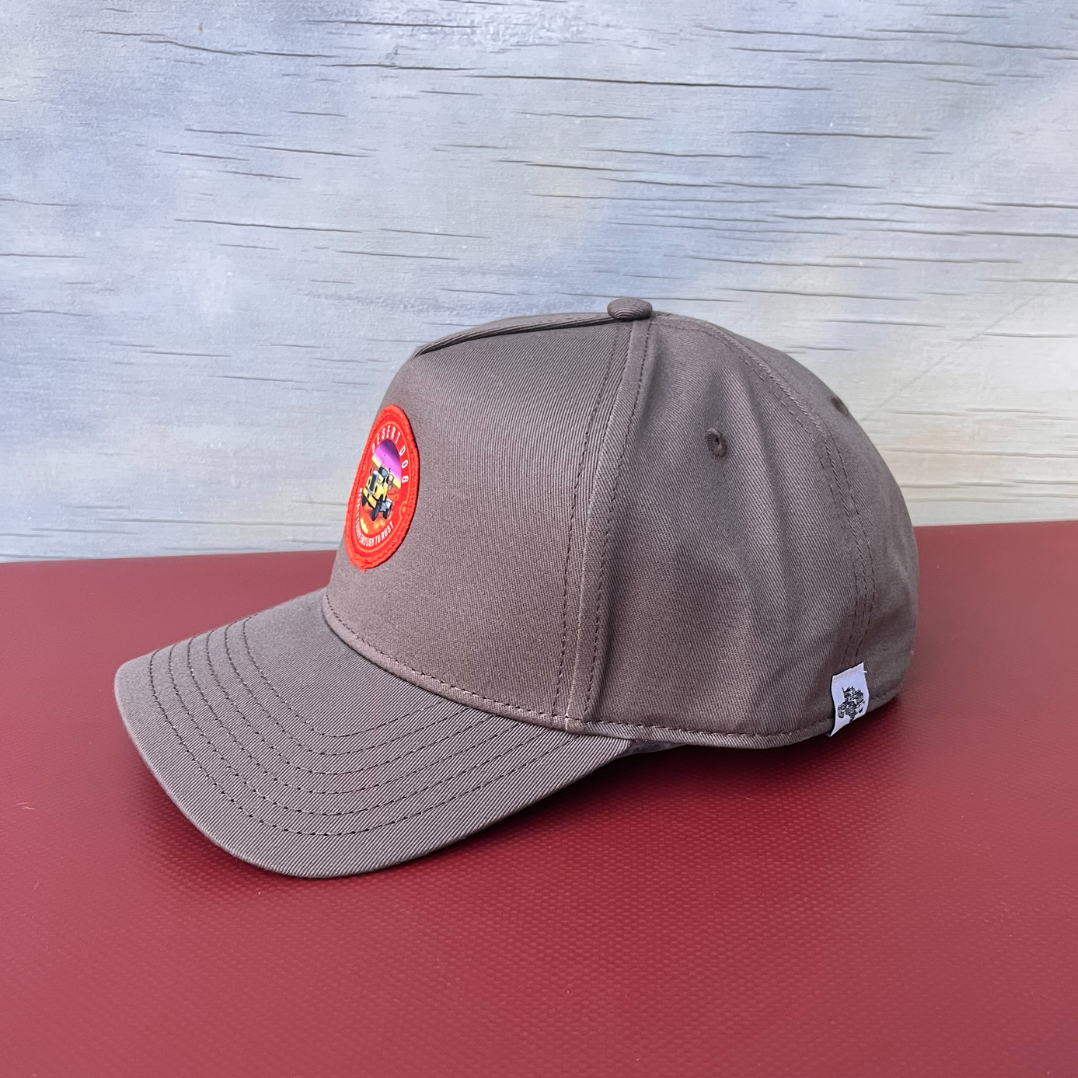 Side view of a walnut coloured high rise cotton cap with a curved peak and featuring the Desert Dog logo