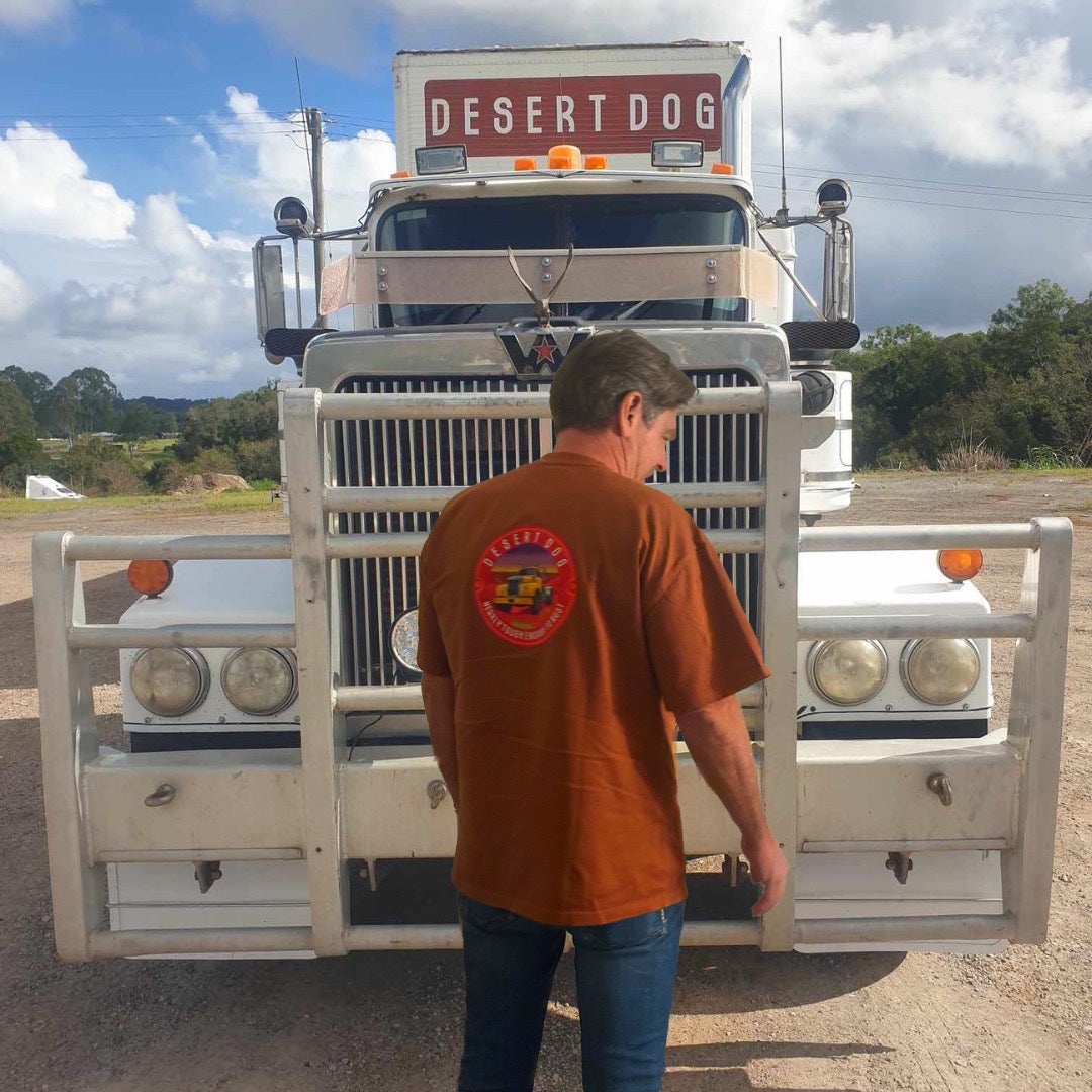 A man stands in front of the Desert Dog Western Star wearing a rust coloured Desert Dog Tough Tshirt with the logo on the back. 