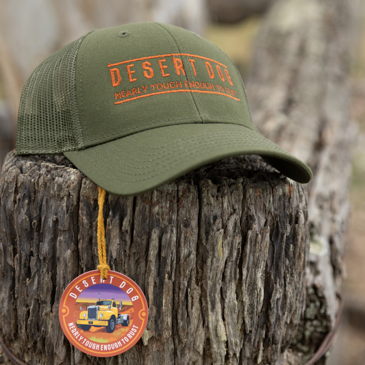 A green curved peak cap perched on a frnce post embroidered with the Desert Dog text logo