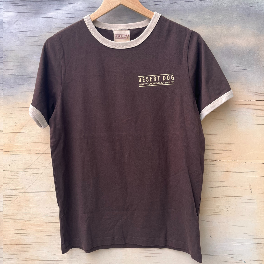 Front view of a brown ringer style tshirt featuring cream binding on the sleeves and neck. There is a small screen print on the left hand chest area that says "Desert Dog - nearly tough enough to rust".