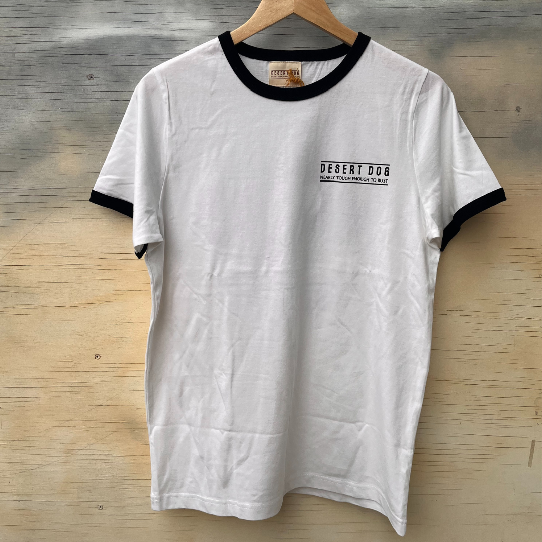 Front view of a white ringer style tshirt featuring black binding on the sleeves and neck. There is a small screen print on the left hand chest area that says "Desert Dog - nearly tough enough to rust".