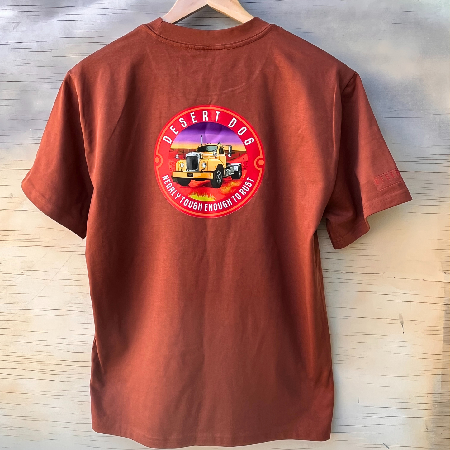 The back of a heavy weight men's t-shirt in rust colour and featuring the Desert Logo log with a B model Mack and the slogan "almost tough enough to rust". 