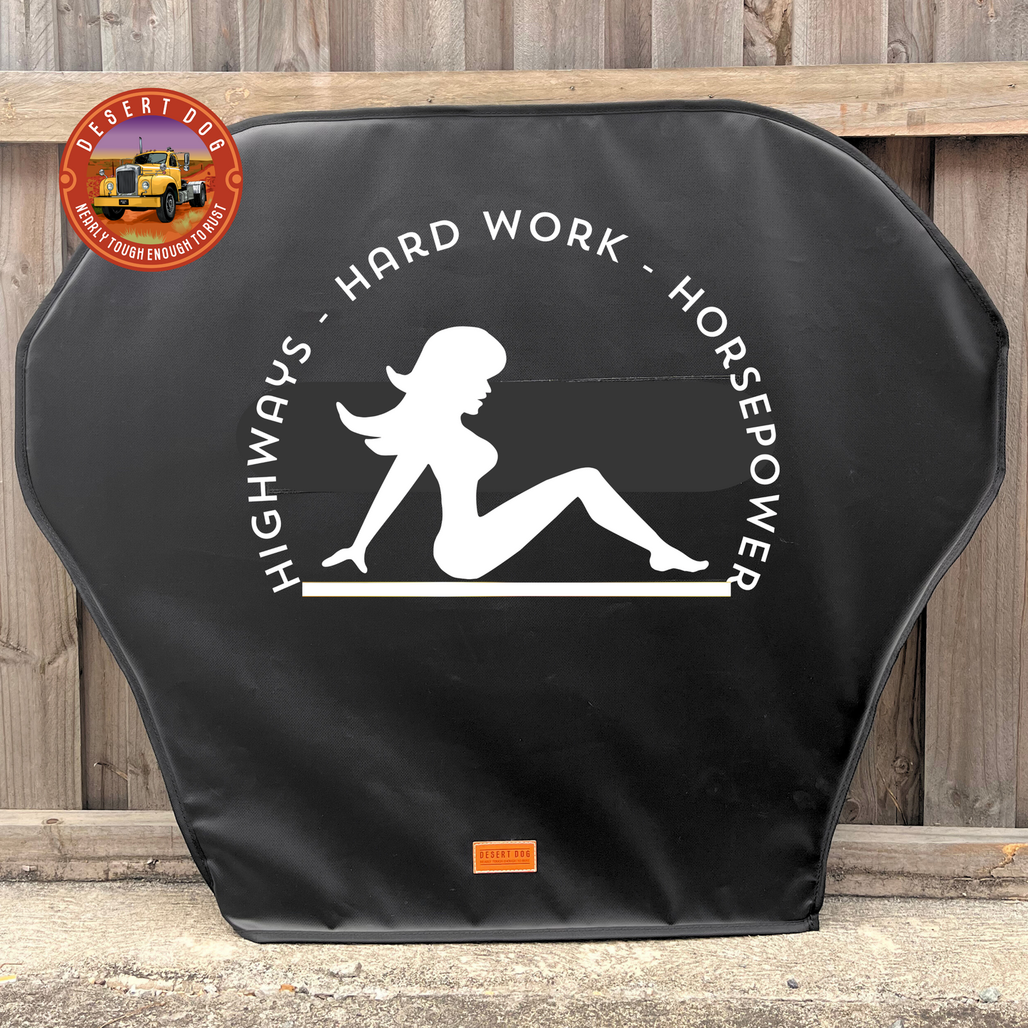 Black cover with white Mudflap Girl and  the words @Highways' Hard work; Horsepower, leaning against a wooden fence