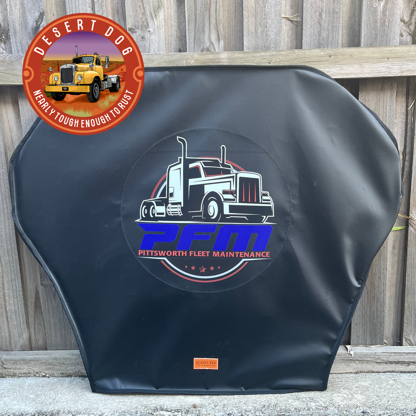 A black custom turntable cover featuring the Pittsworth Fleet Maintenance (PFM) logo, leaning against a paling fence.