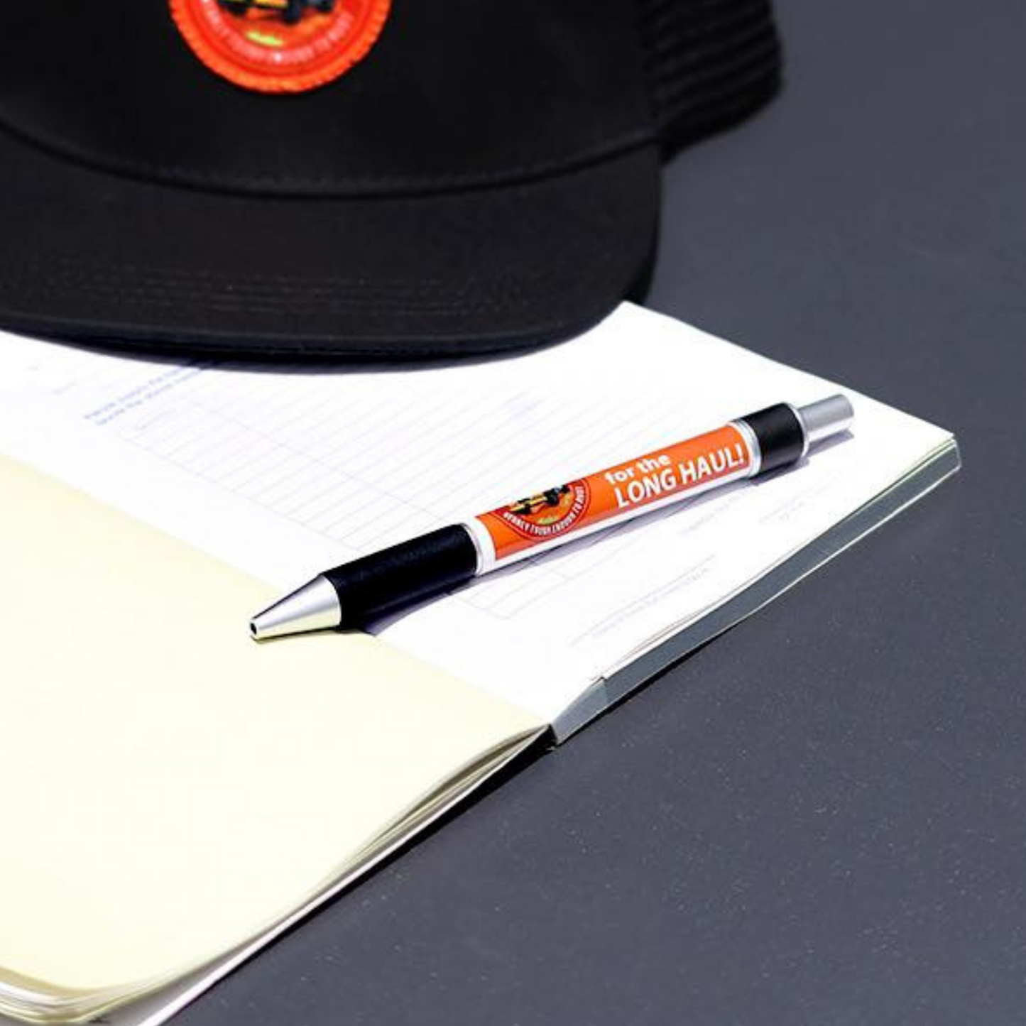 A Desert Dog pen laying across a blank notebook with a cap in the background