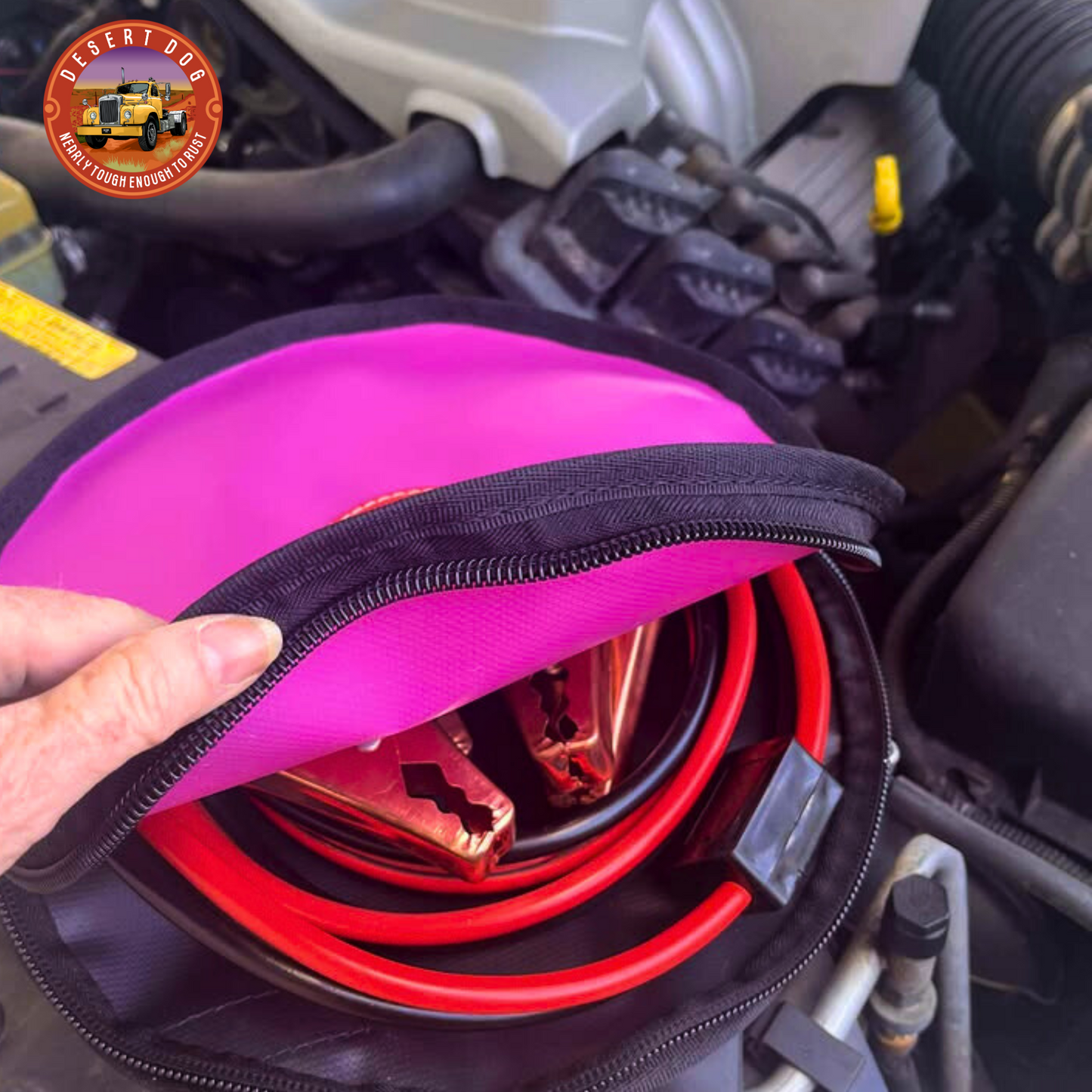 Pink 30cm Desert Dog rope bag with jump leads coiled inside and visible through the opened zip of the bag. The bag is sitting in the engine bay of a V6 holden 