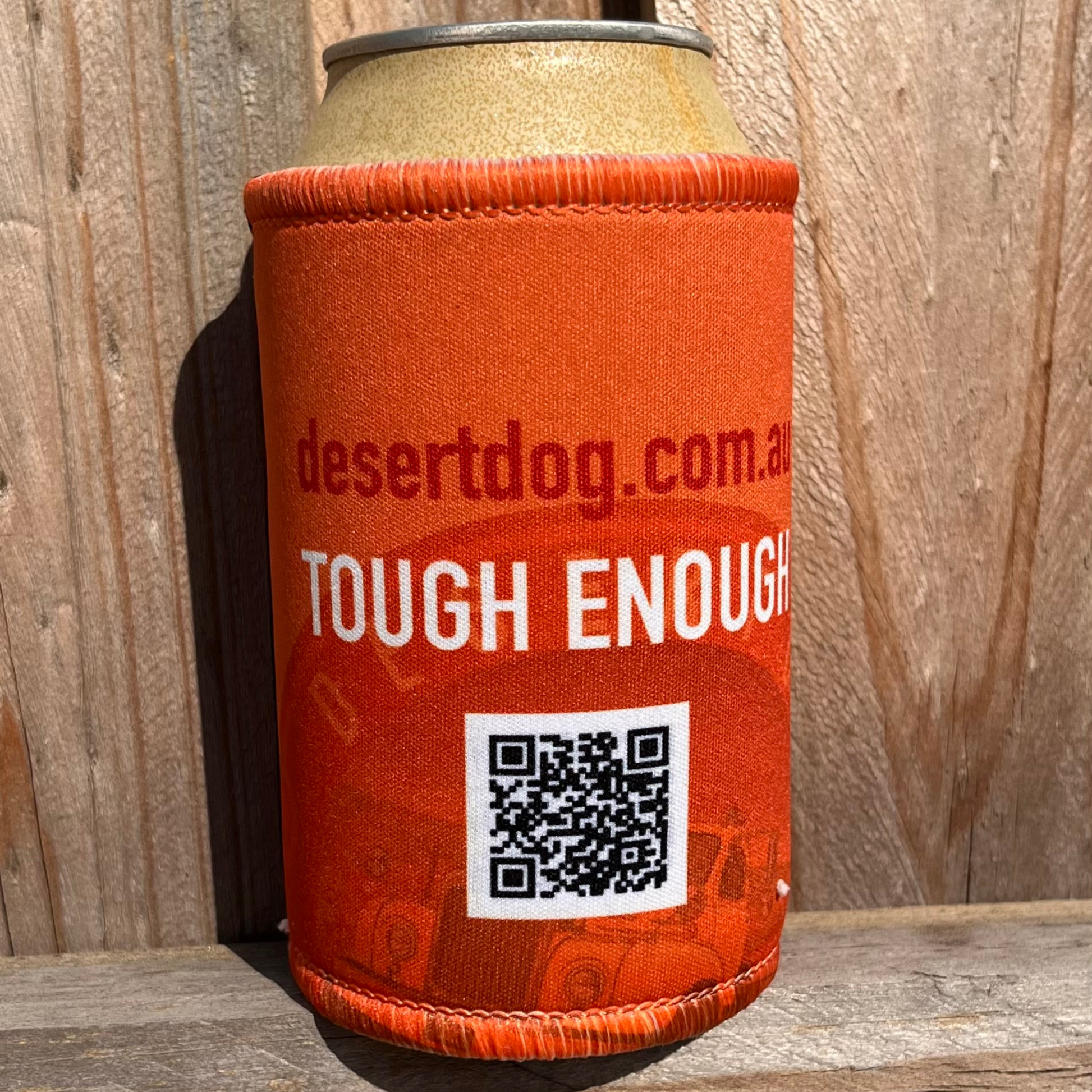 Back view of the signature orange stubby holder with the Desert Dog Facebook QR code and the words Tough Enough, sitting on a wooden fence