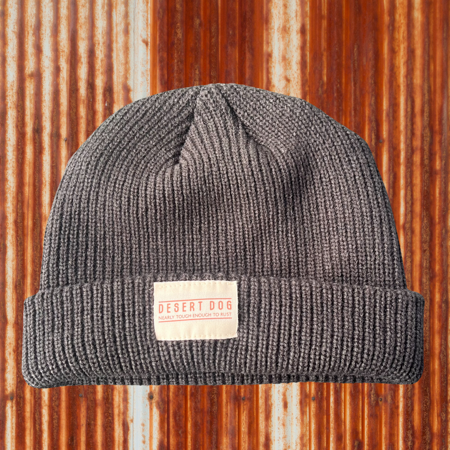 Slate coloured beanie labelled Desert Dog, nearly touch enough to rustwith a rusty tin wall background 