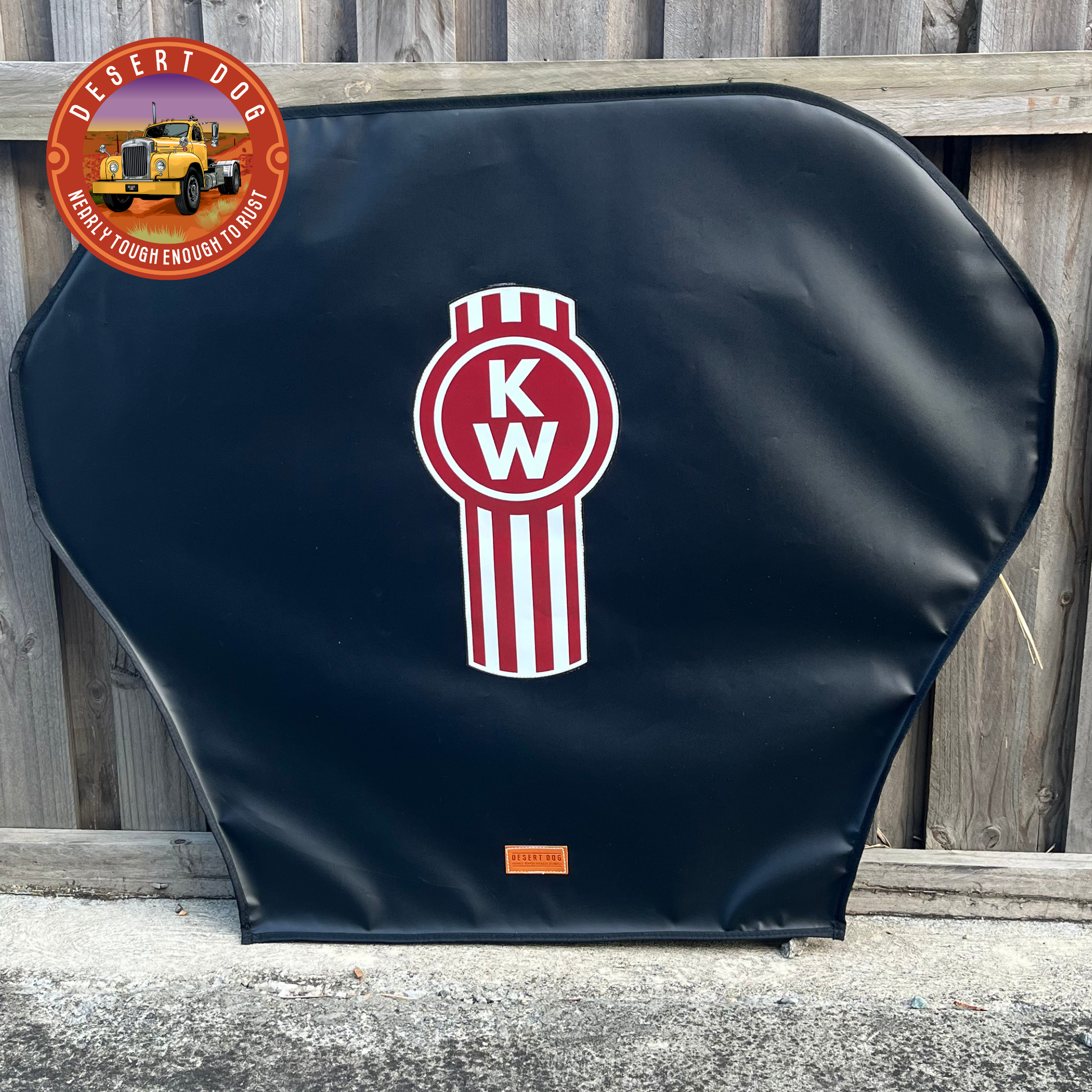 A black turntable cover leaning against a paling fence and featuring the Kenworth logo