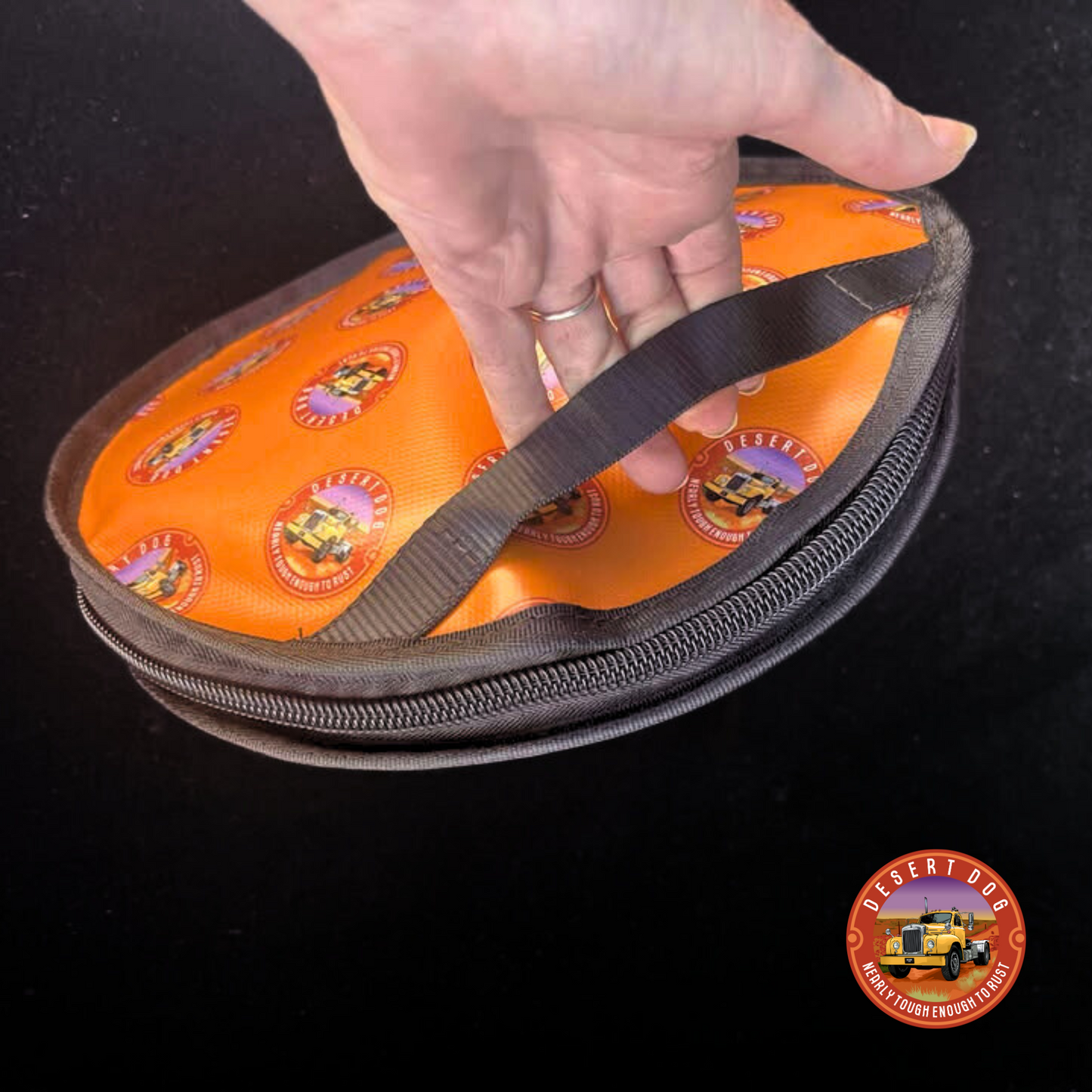 Hand holding an orange Rope bag with the Desert Dog allover logo design. The focus of the photo is to showcase the easy grab carry handle.